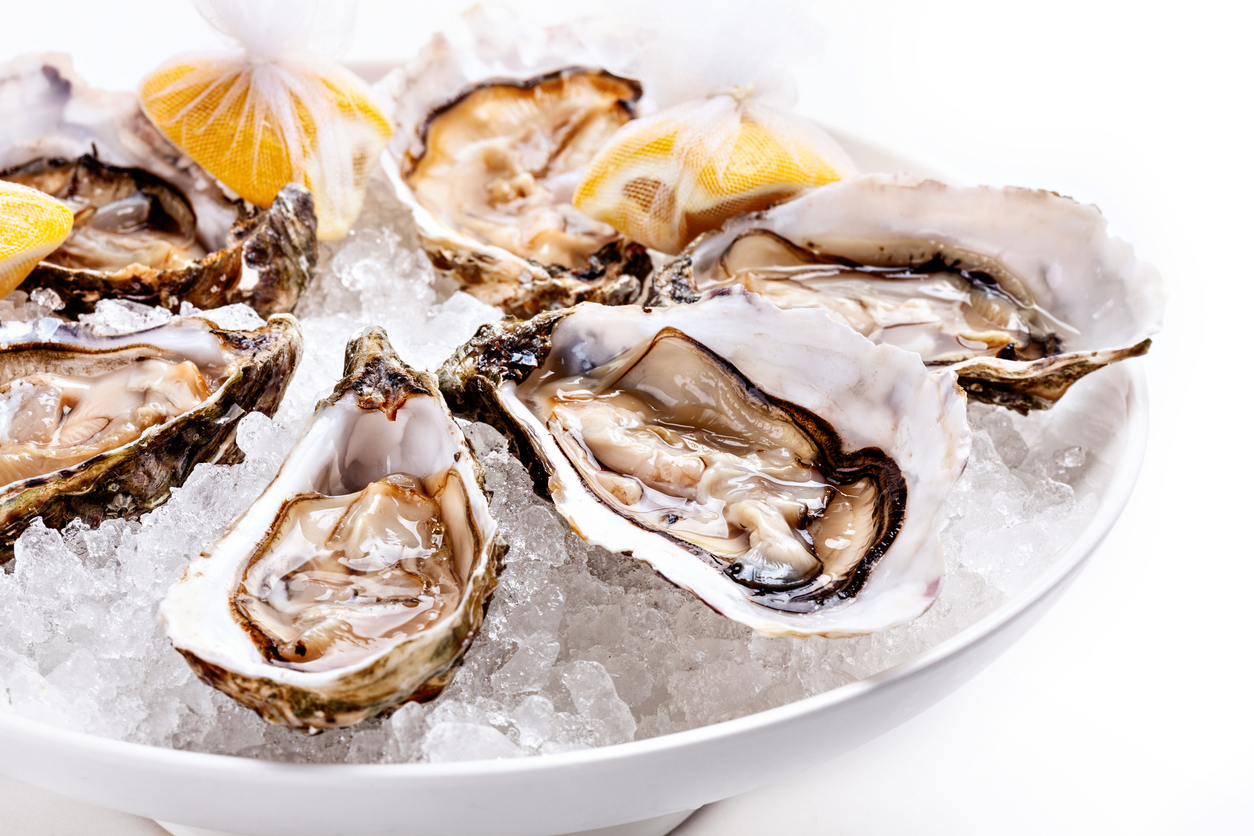 Half dozen fresh oysters are served with lemon in bowl with plenty of ice. White background Close up.