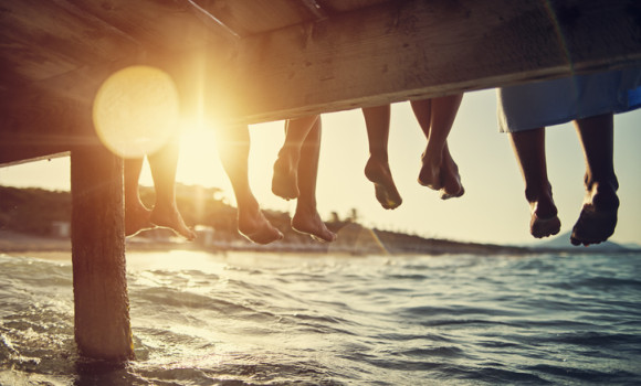 Five people having fun sitting on pier. Feet shot from below the pier. Sunny summer day evening.