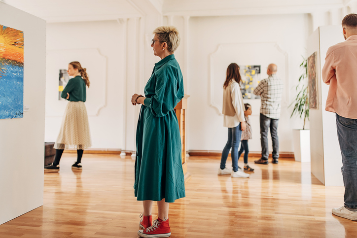 Diverse group of visitors in modern art gallery looking at paintings