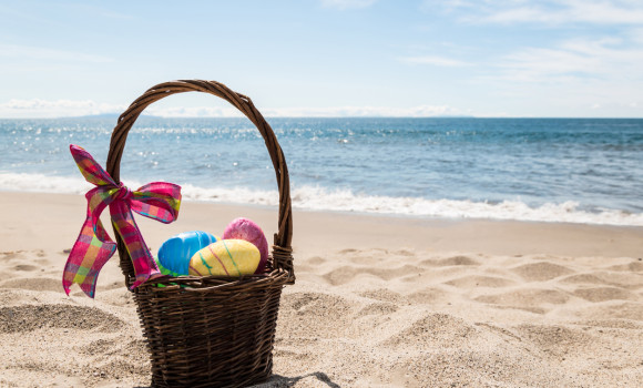 Easter basket with color eggs on the sandy beach near ocean