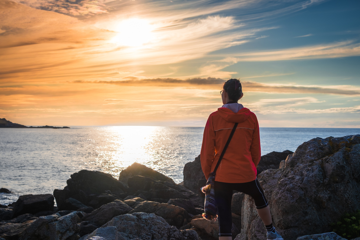 Woman watching beautiful sunset over ocean from rugged shoreline